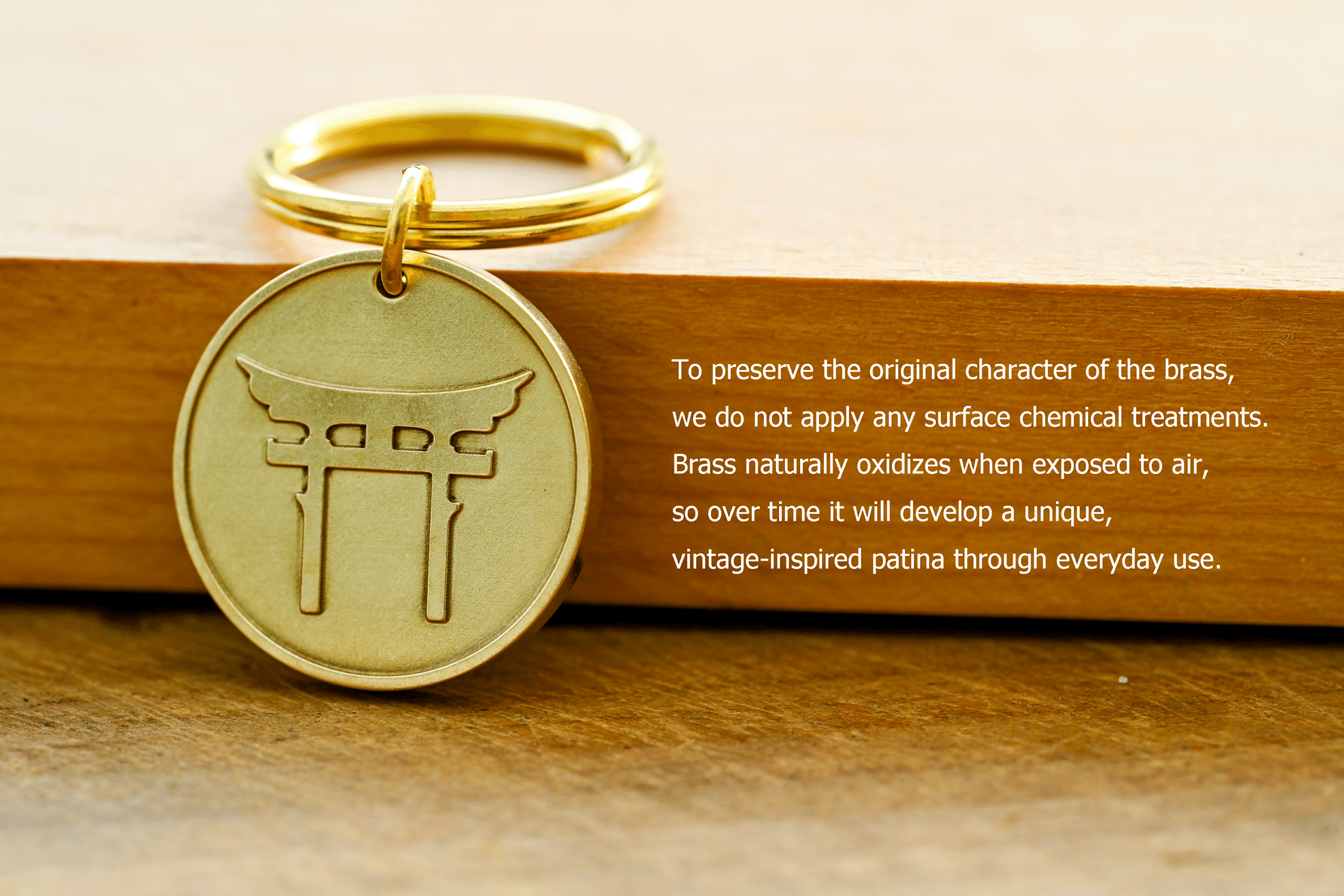 Brass keychain tag with an engraved torii gate. Text: To preserve the original character of the brass, we do not apply any surface chemical treatments. Brass naturally oxidizes when exposed to air, so over time it will develop a unique, vintage-inspired patina through everyday use