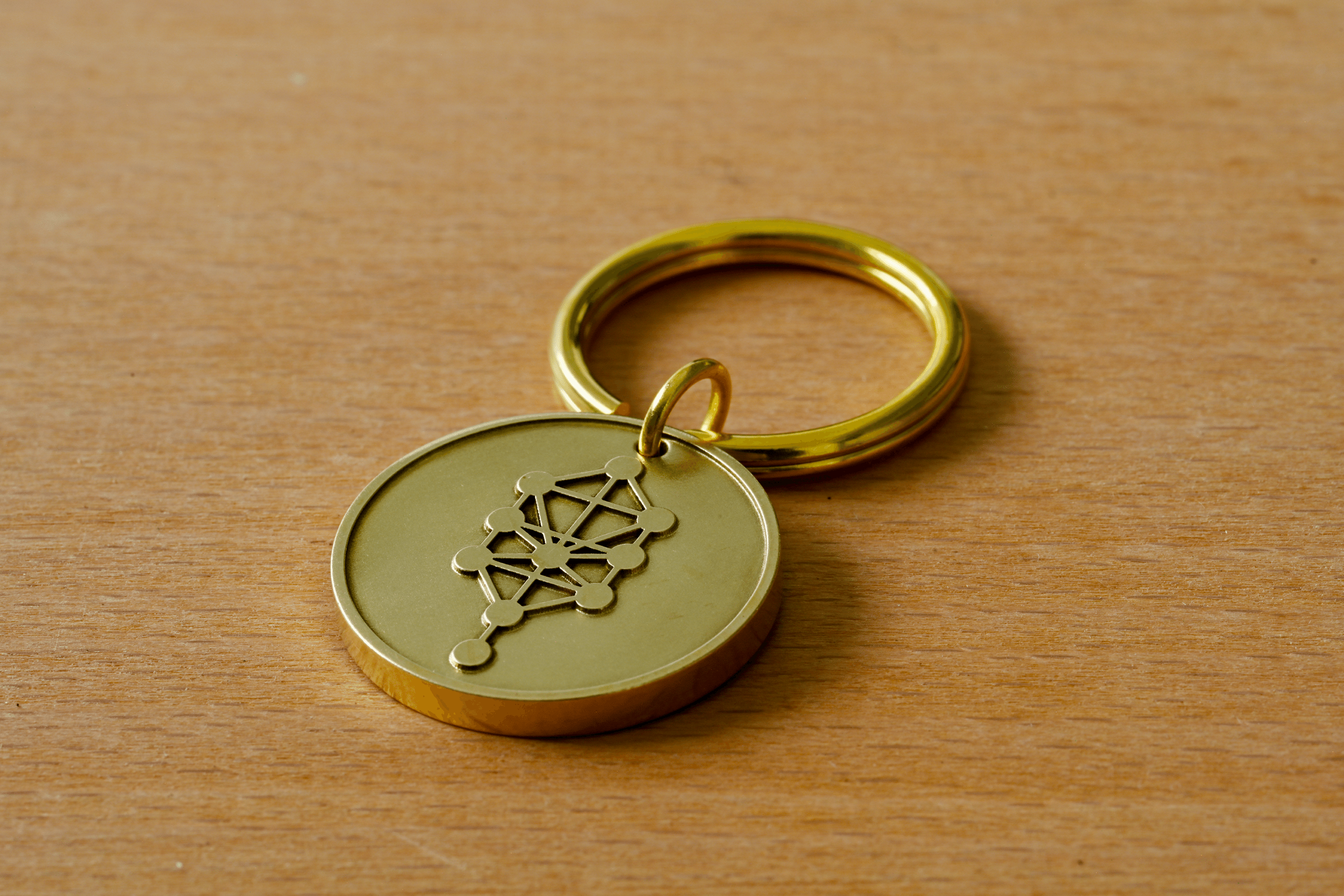 Gold keychain medallion engraved with the Kabbalah Tree of Life symbol on a wooden surface