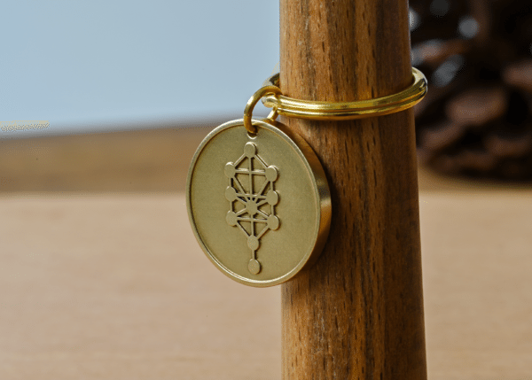Brass keychain charm engraved with the Kabbalah Tree of Life symbol hanging on a wooden post
