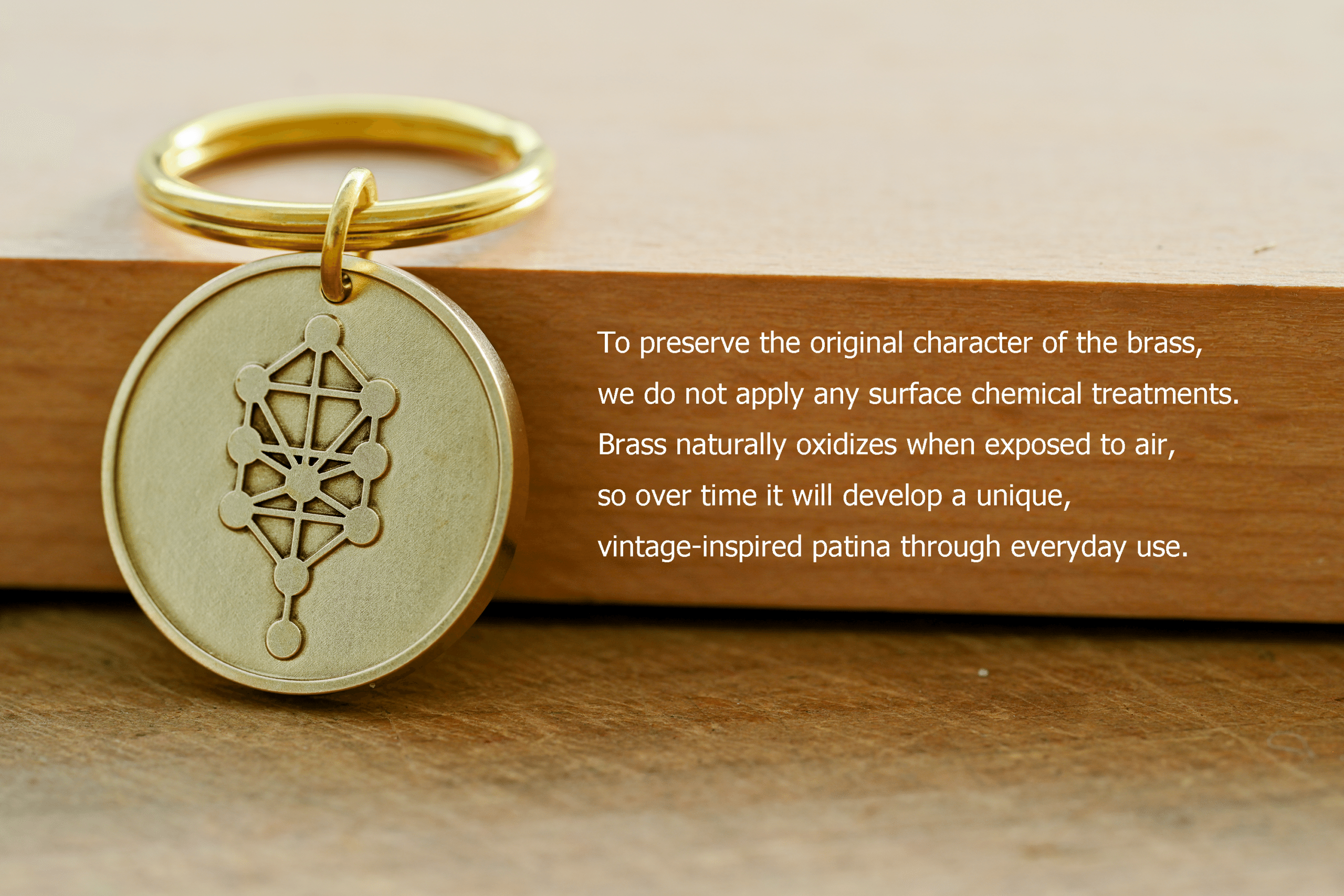 Brass Tree of Life keychain medallion beside text: To preserve the original character of the brass, we do not apply any surface chemical treatments. Brass naturally oxidizes when exposed to air, so over time it will develop a unique, vintage-inspired patina through everyday use