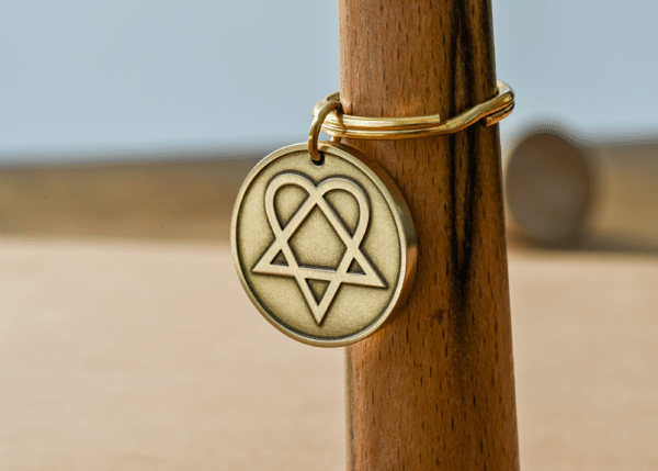 Brass circular keychain tag featuring an engraved heartagram symbol hanging on a wooden post