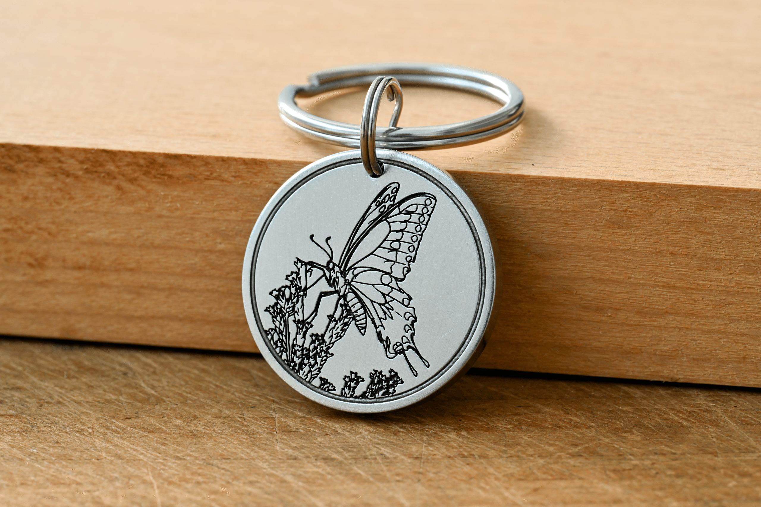 Silver round keychain tag engraved with a butterfly resting on flowers