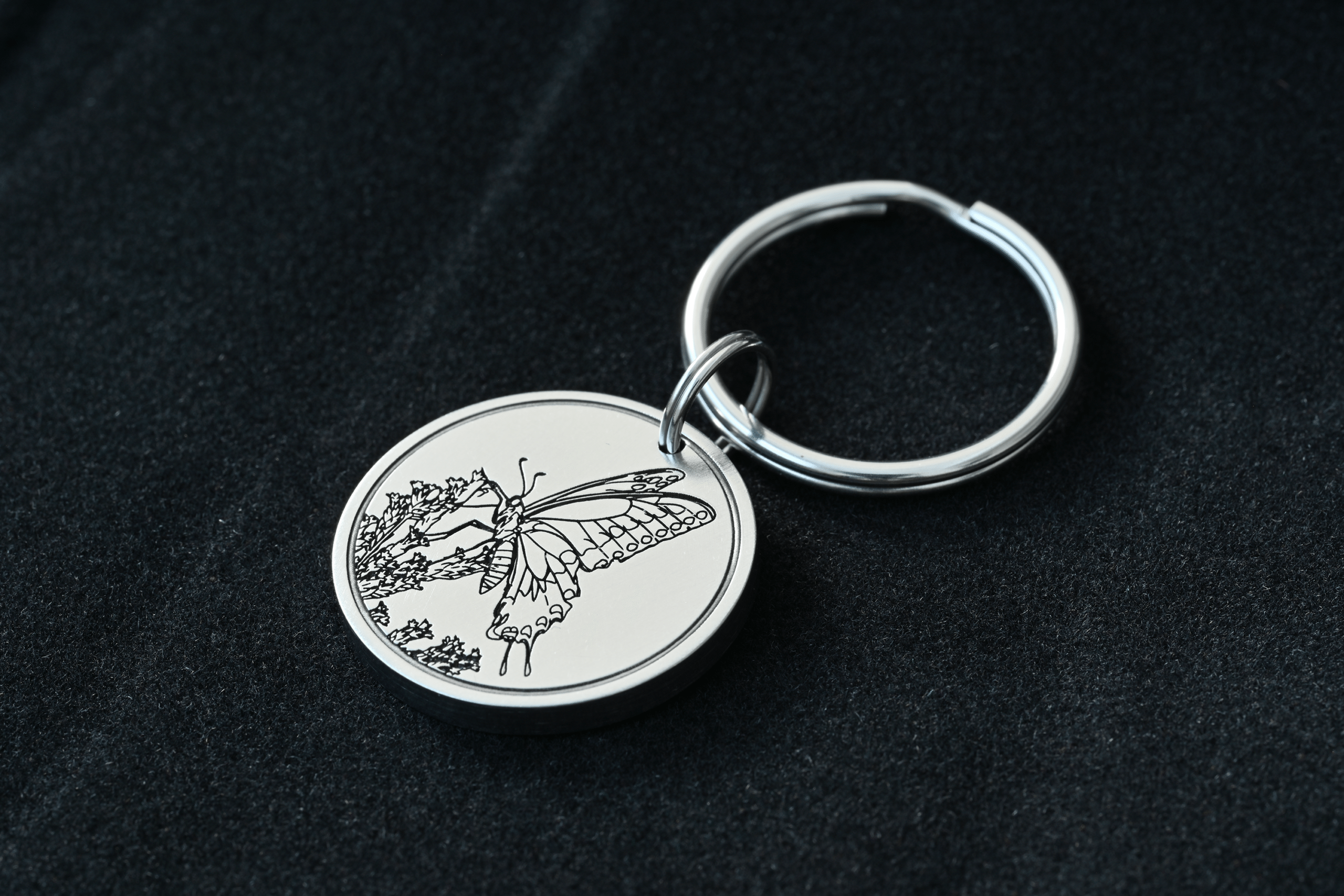 Silver circular metal keychain engraved with a detailed butterfly resting on a plant