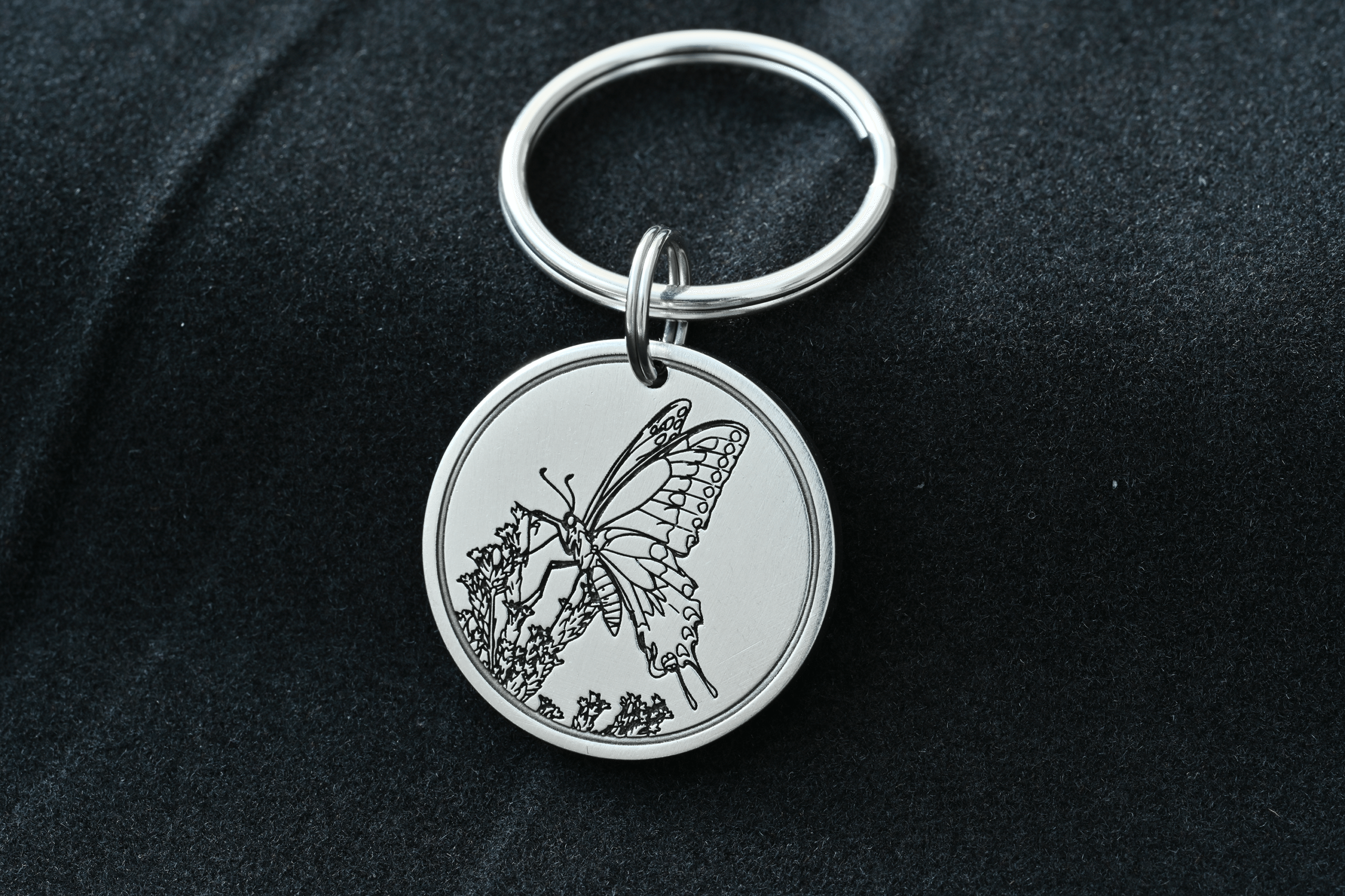 Silver round keychain tag engraved with a detailed butterfly resting on flowers