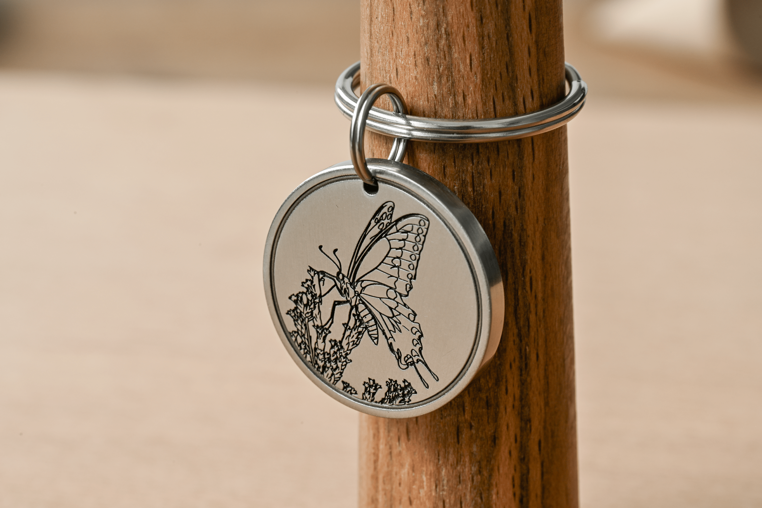 Round silver metal tag engraved with a detailed butterfly resting on flowers