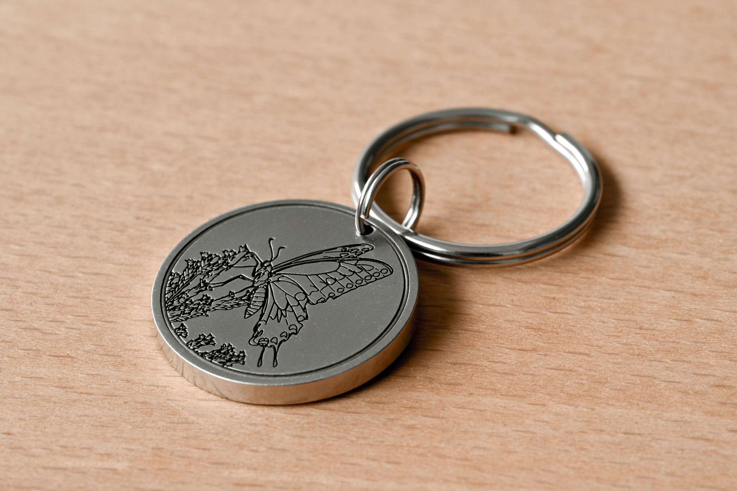 Silver circular keychain tag with an engraving of a butterfly on flowers