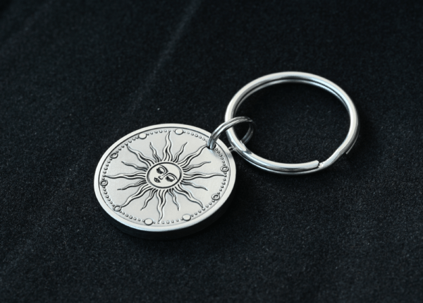 Silver keychain with a circular metal pendant engraved with a celestial sun face