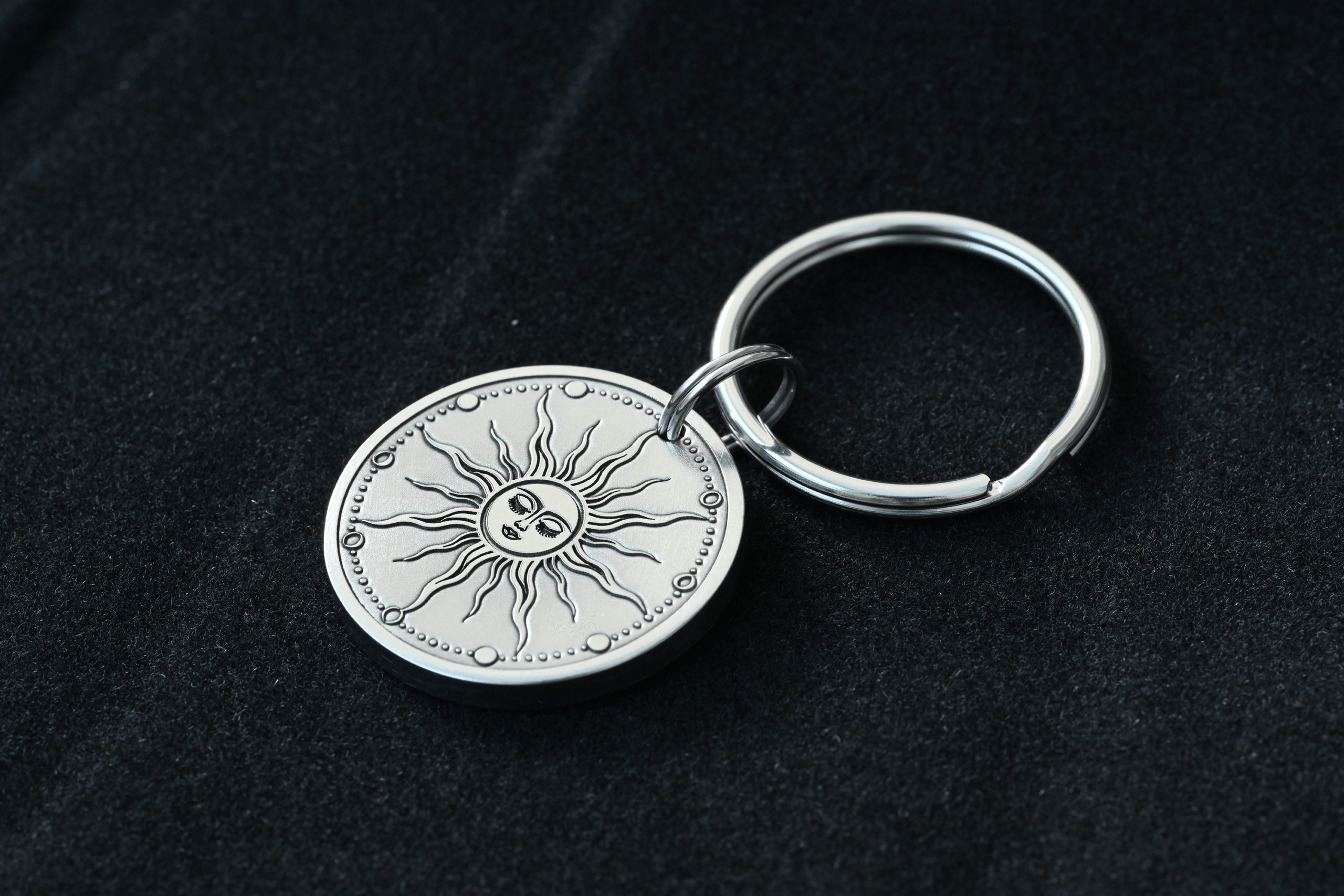 Silver keychain with a circular metal pendant engraved with a celestial sun face
