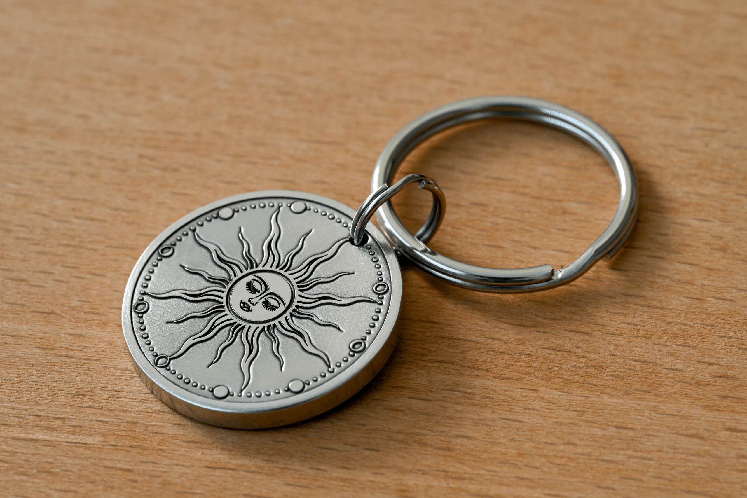 Silver round keychain featuring an engraved celestial sun with a face, resting on a wooden surface