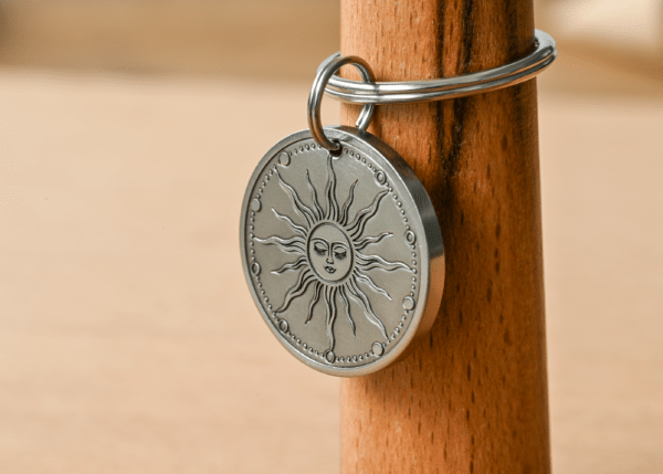 Round silver metal tag engraved with a celestial sun face and radiating rays