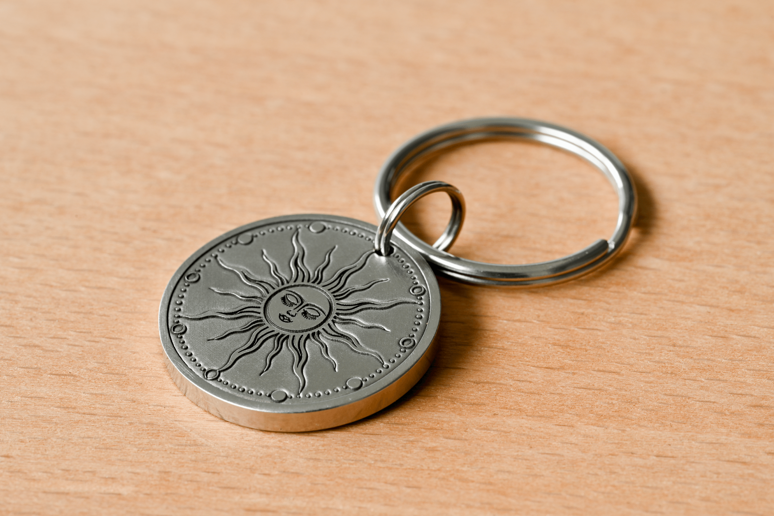 Silver medallion keychain engraved with a celestial sun face resting on a wooden surface