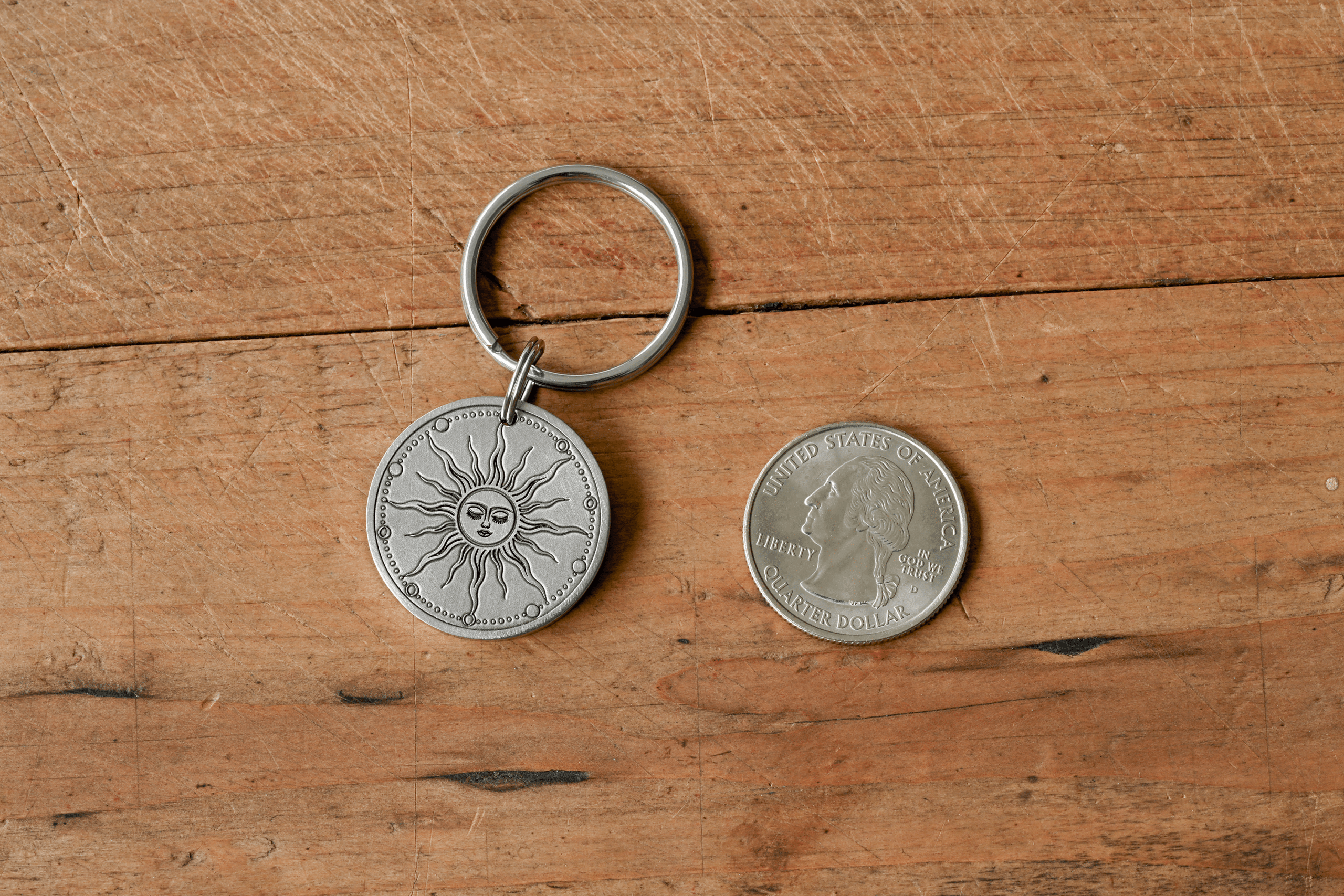 Silver celestial sun keychain pendant next to a US quarter for size comparison